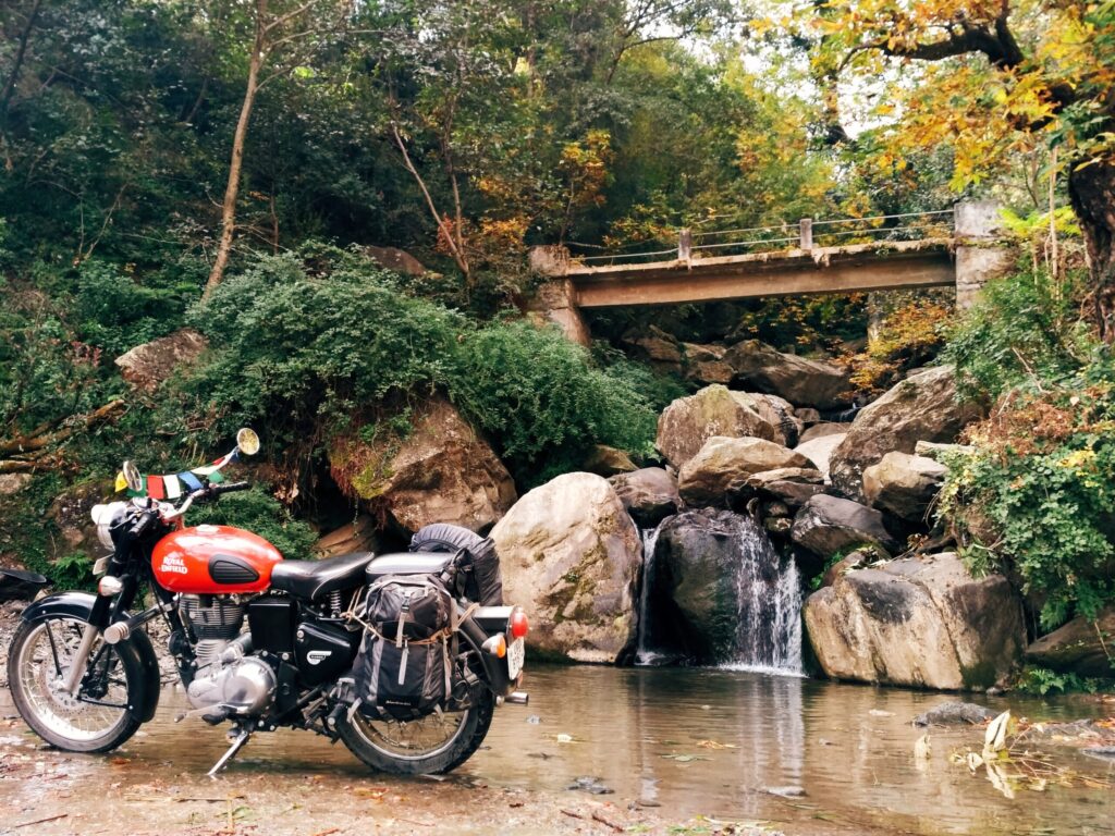 red motorcycled parked beside rocks with flowing waters during daytime